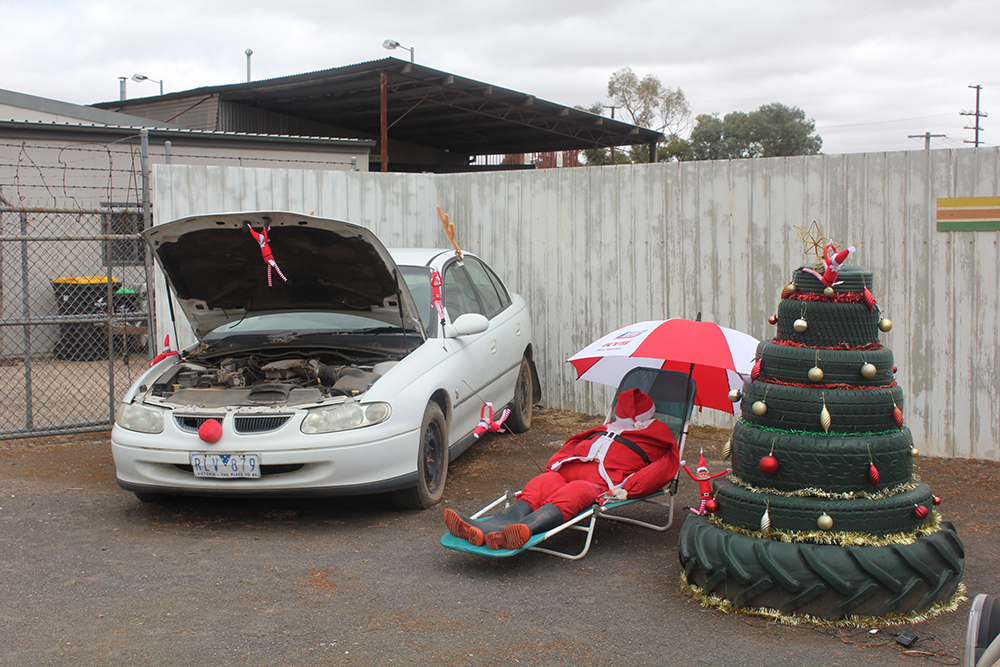 Christmas tree made out of tyres and a santa sitting in a chair and a car with a red nose on front.