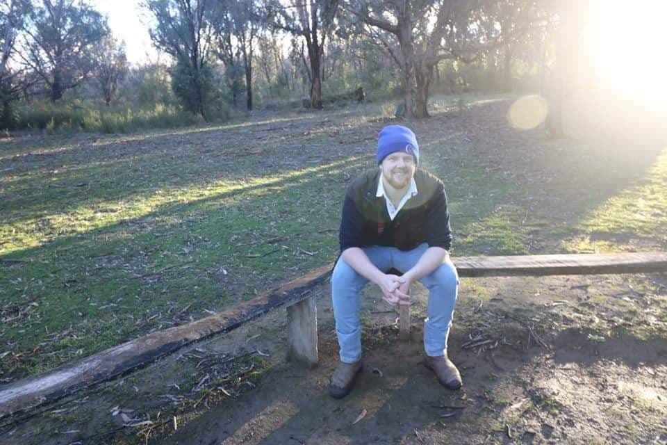 Rory Speirs sitting on a wooden bench smiling.